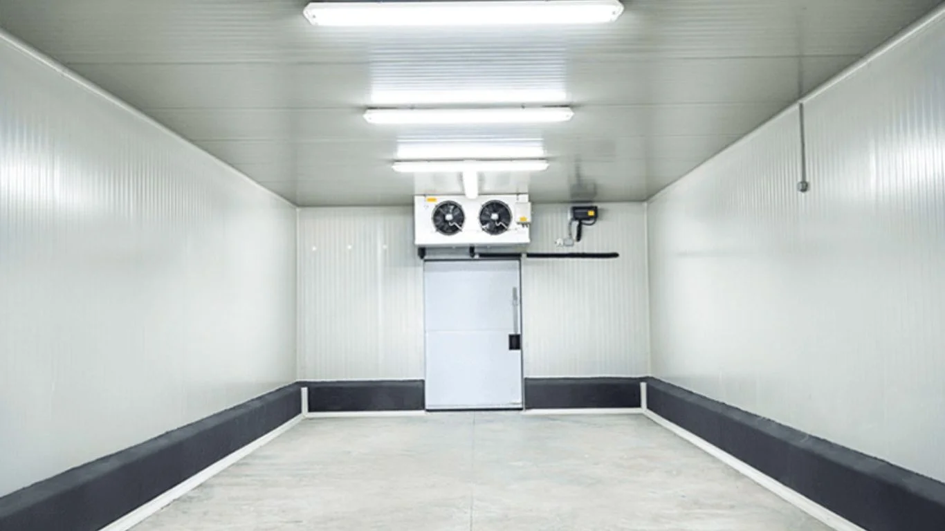 Empty insulated-panel cold room with ceiling evaporator unit above a sliding cold-room door